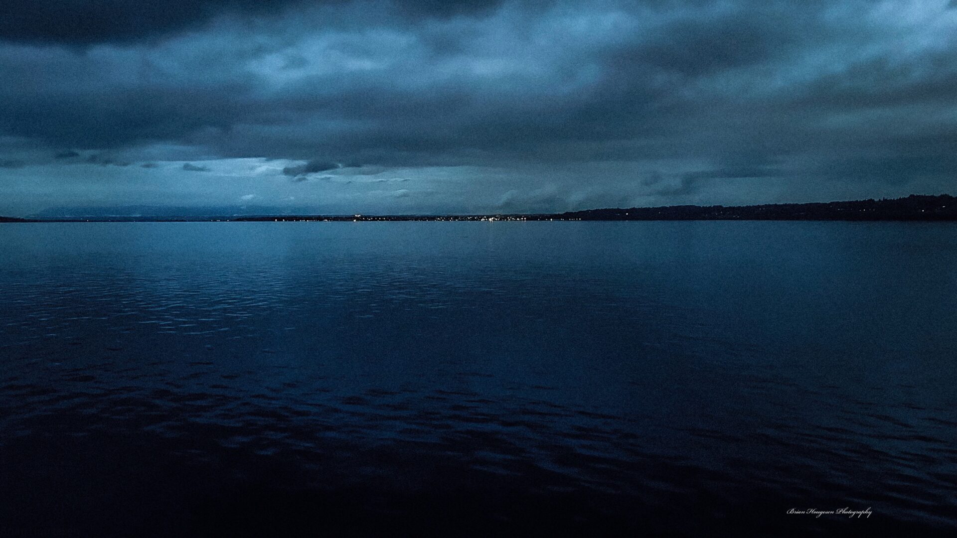 A dark sky over the ocean with lights on.