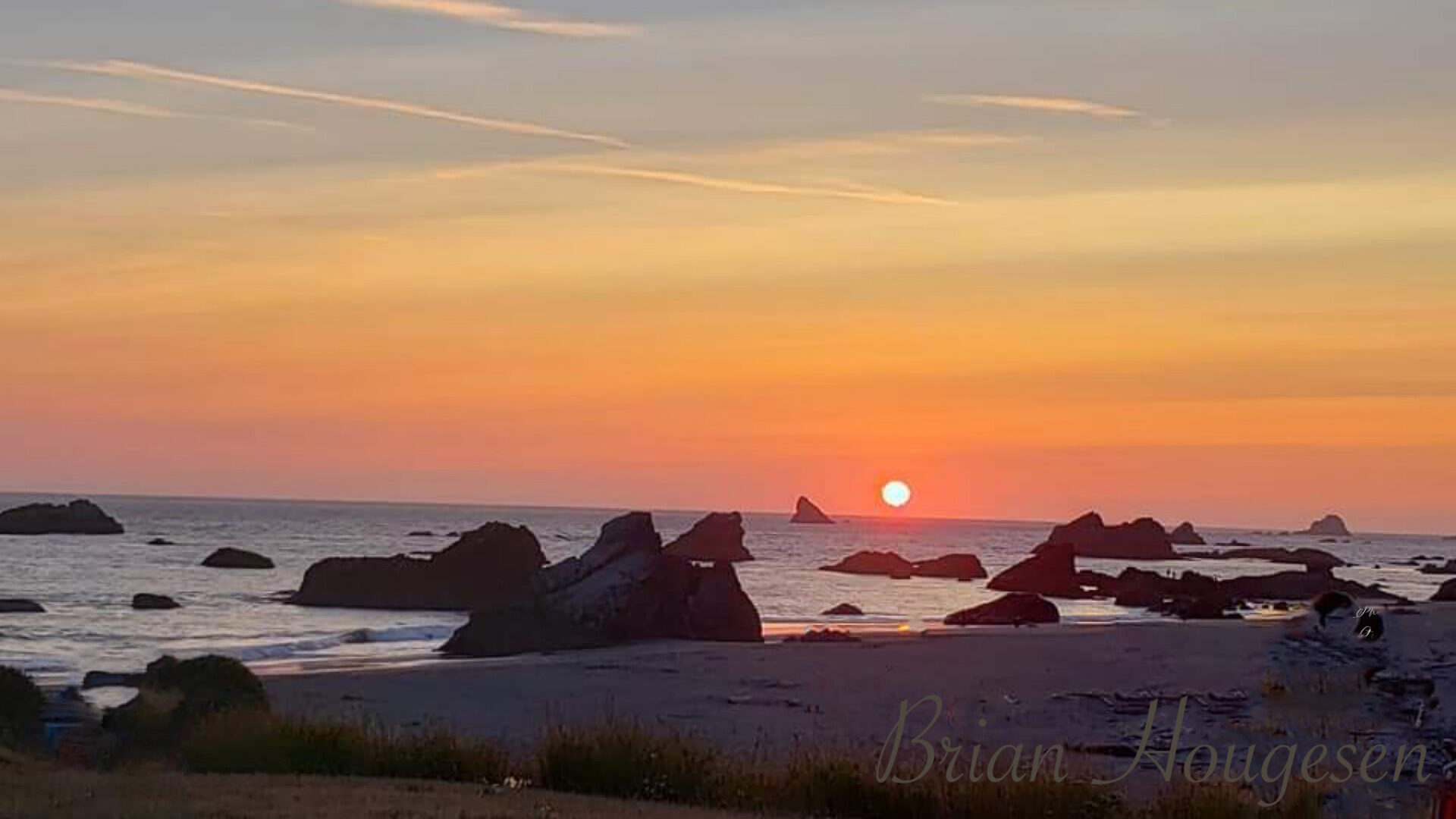 A sunset over the ocean with rocks in the foreground.