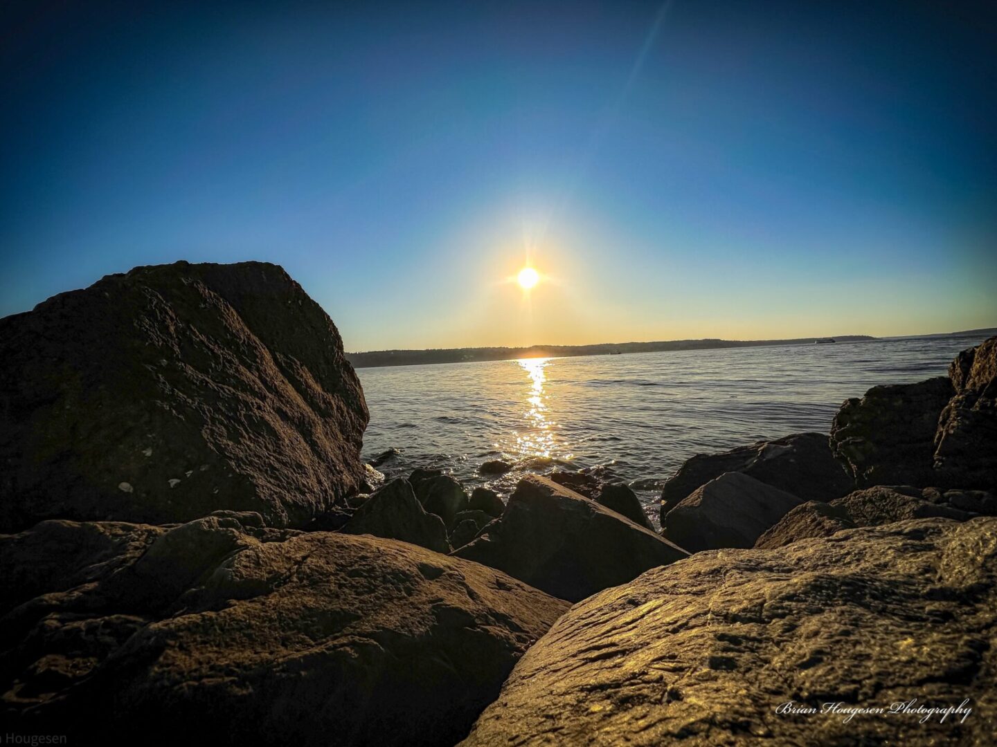 A sunset over the ocean with rocks in front of it.