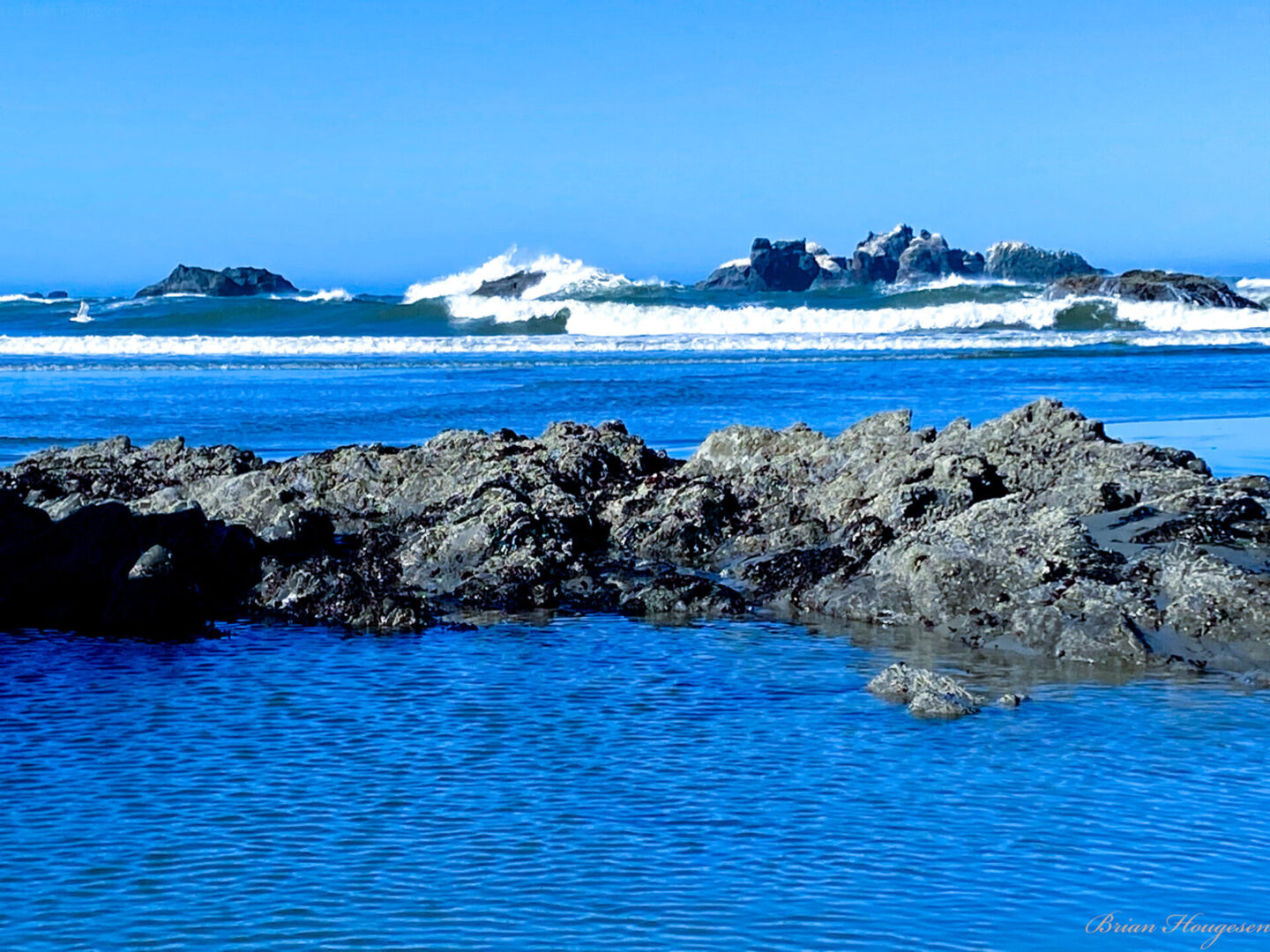 A body of water with rocks in the foreground and waves crashing on shore.